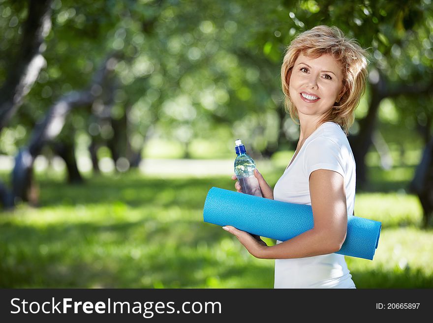Mature woman in a park with a bottle and gym mat. Mature woman in a park with a bottle and gym mat
