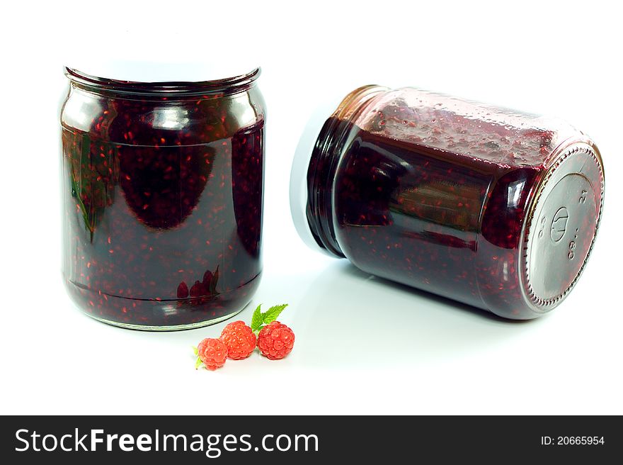 Jars of homemade raspberry jam and a few raspberries / white background