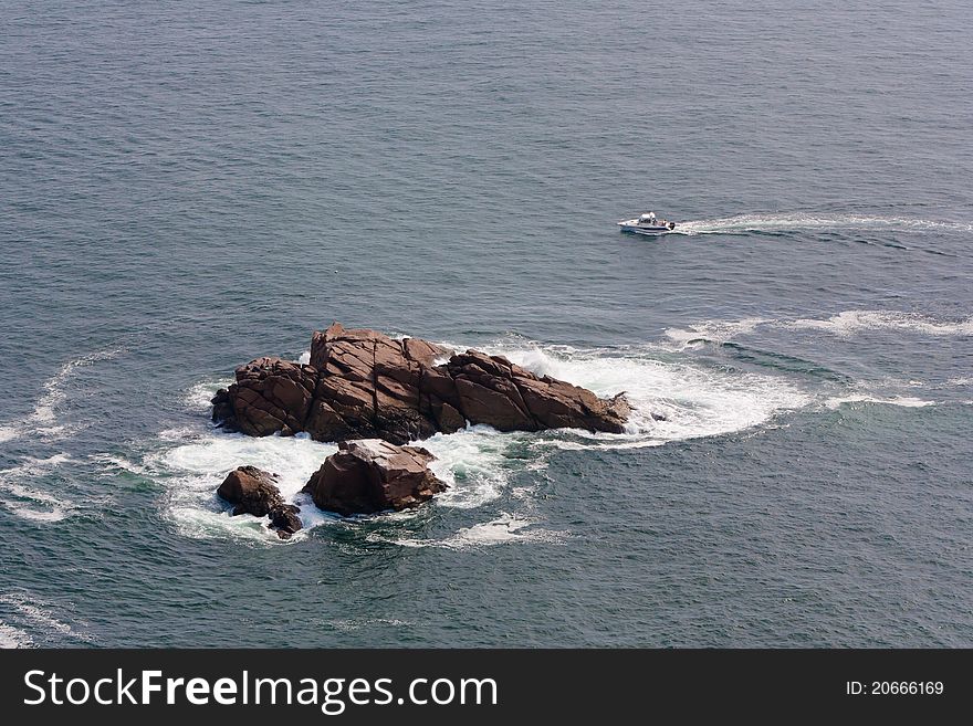 An isolated piece of rock in the Atlantic Ocean near Cabo da Roca, Portugal. A recreational boat approaching the rock. An isolated piece of rock in the Atlantic Ocean near Cabo da Roca, Portugal. A recreational boat approaching the rock.