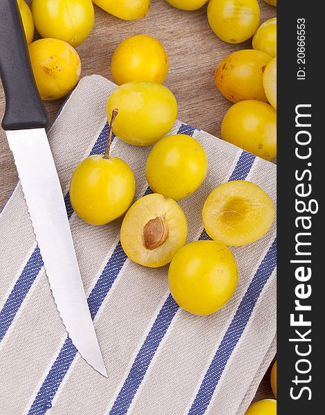 Studio-shot of small yellow plums also known as mellow mirabelles, on a dishtowel. one is halved with a knife.