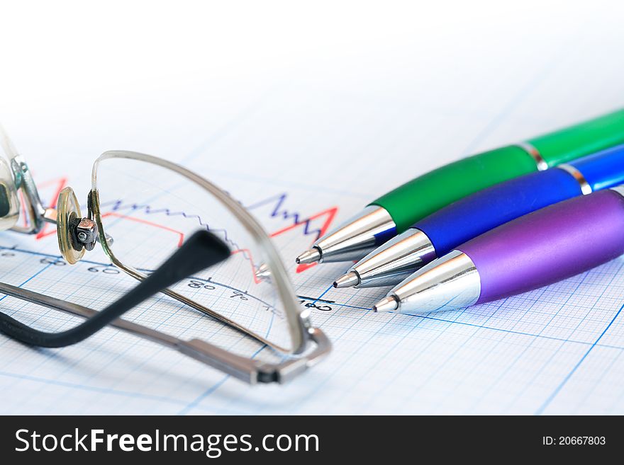 Extreme closeup of few color pens near spectacles on graph paper background with diagram. Extreme closeup of few color pens near spectacles on graph paper background with diagram