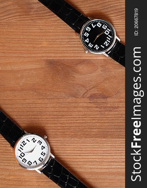Pair of modern black and white wristwatches on wooden surface