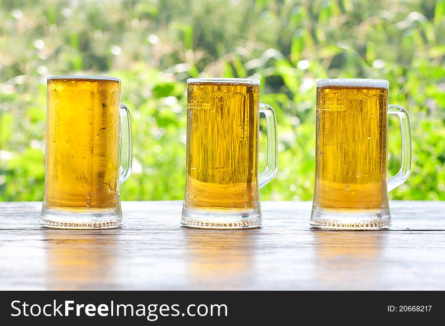 Three mug of beer at the table close-up, background is out of focus