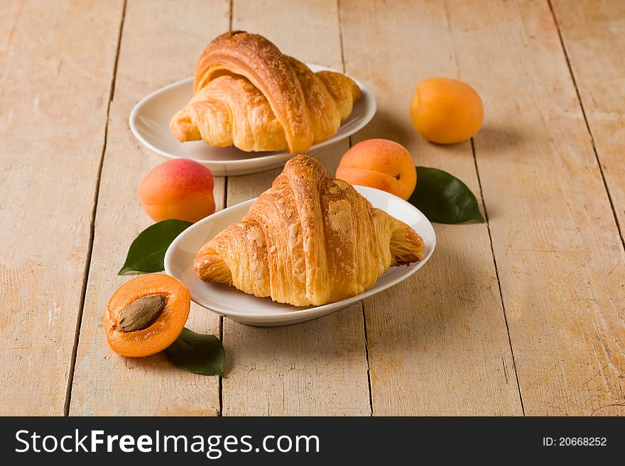 Photo of delicious golden croissants with apricot marmalade on wooden table