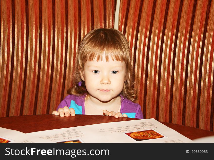 Little girl sitting in a cafe and looking at menu. Little girl sitting in a cafe and looking at menu