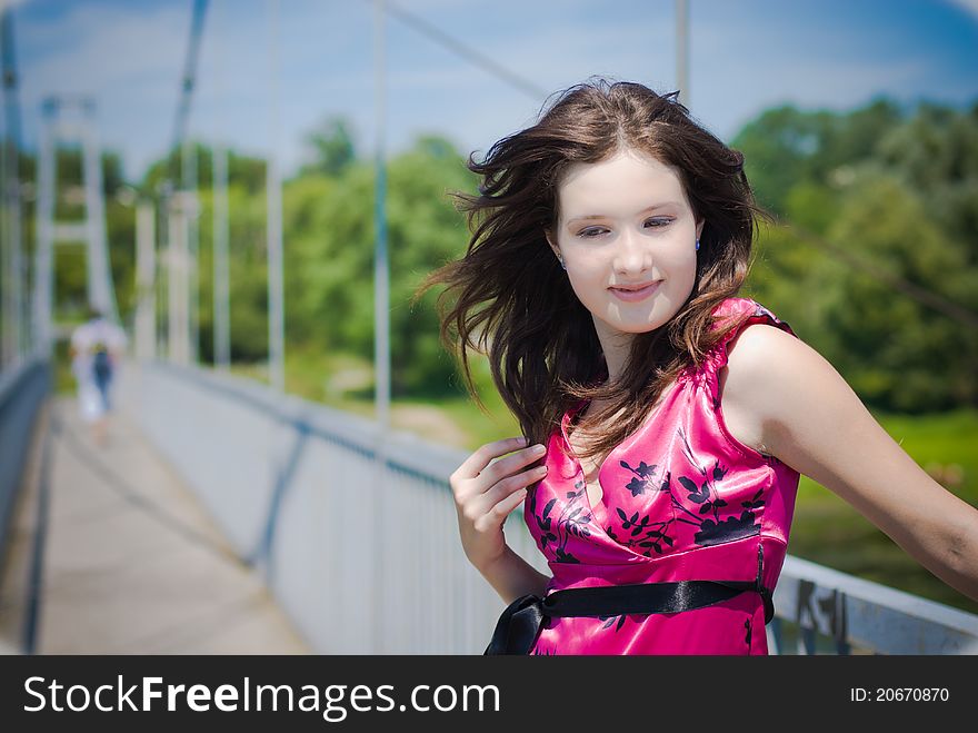 Young girl in bright pink dress on bridge with a man going away on background. Young girl in bright pink dress on bridge with a man going away on background