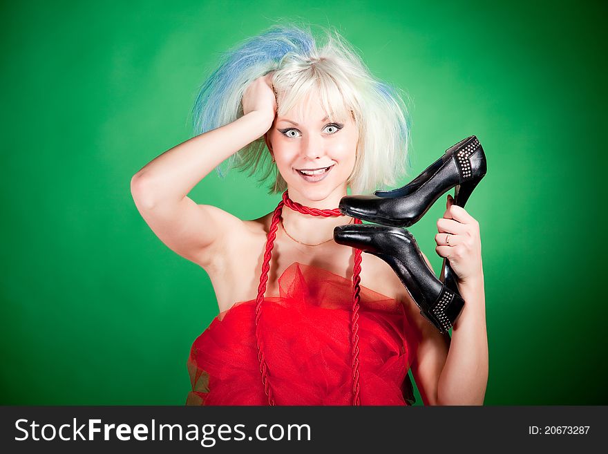 Blonde crazy girl holding shoes, portrait shot over green background