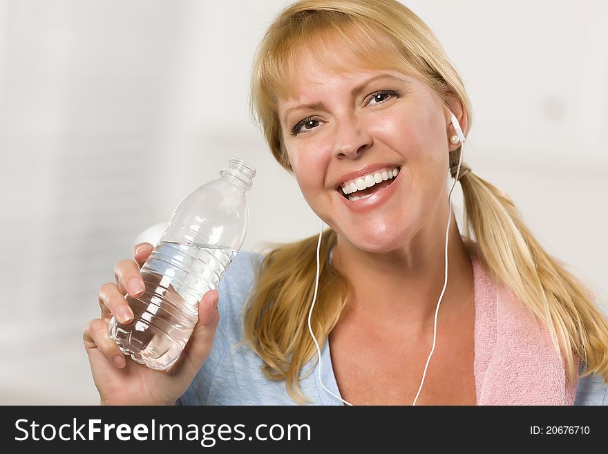 Pretty Blonde Woman with Towel and Ear Phones Drinking From Water Bottle in Her Kitchen. Pretty Blonde Woman with Towel and Ear Phones Drinking From Water Bottle in Her Kitchen.