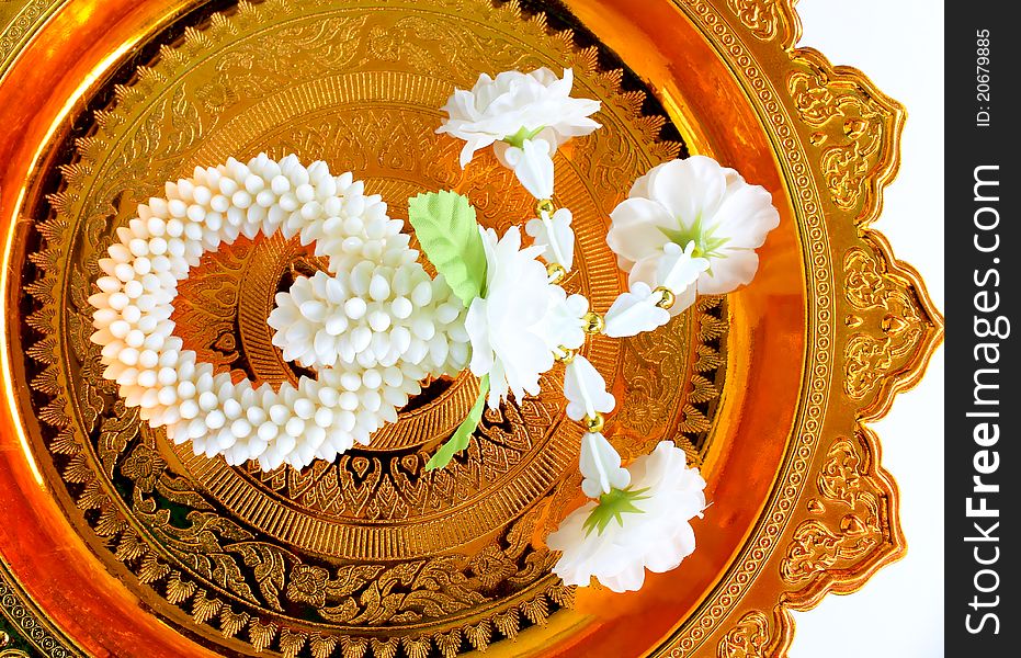 Jasmine garland on gold tray with pedestal, white background.