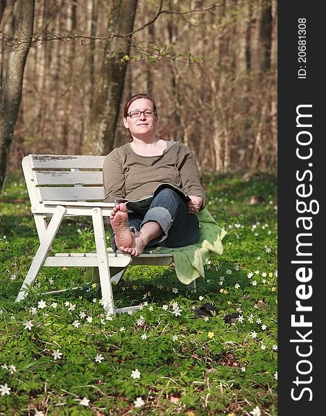 Woman sitting on a sofa in the wood in springtime. She is reading a magazine in the sunlight. Woman sitting on a sofa in the wood in springtime. She is reading a magazine in the sunlight