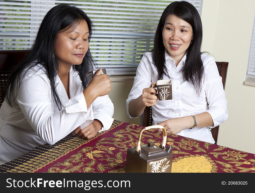 Two Asian women drinking tea sitting at table.