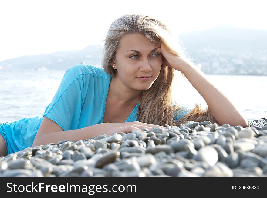 Portrait of a beautiful young woman posing on stones near sea