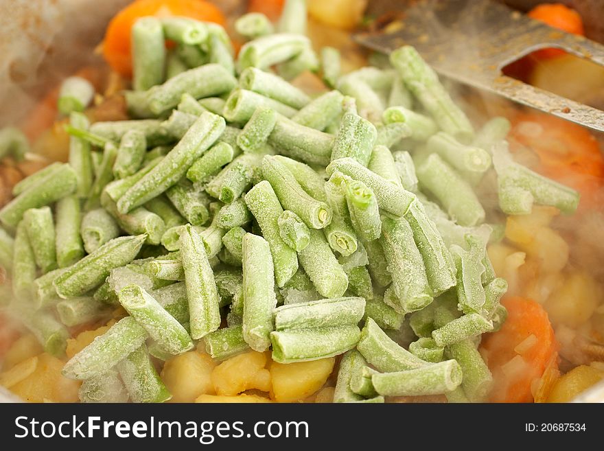 Frozen green beans is added to vegetable stews. Beans straight from the freezer, covered with snow. In the background is visible a metal blade.