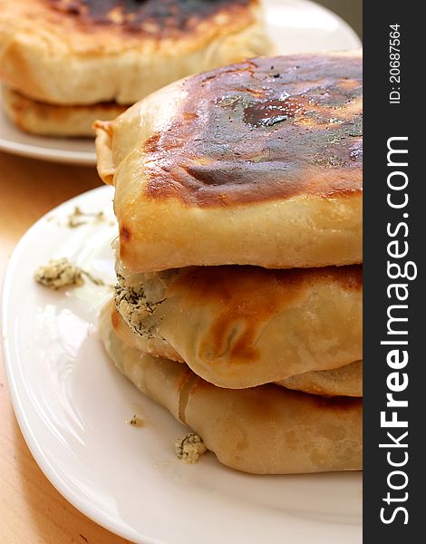 On the plate is a stack of pies. One of the pie filling is broken and fallen. In a stack of three pies. In the background are two more pie on the plate.