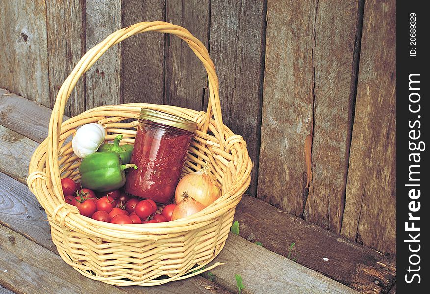 Image of a basket of freshly picked organic vegetables and a jar of homemade salsa on a rustic background. Image of a basket of freshly picked organic vegetables and a jar of homemade salsa on a rustic background.