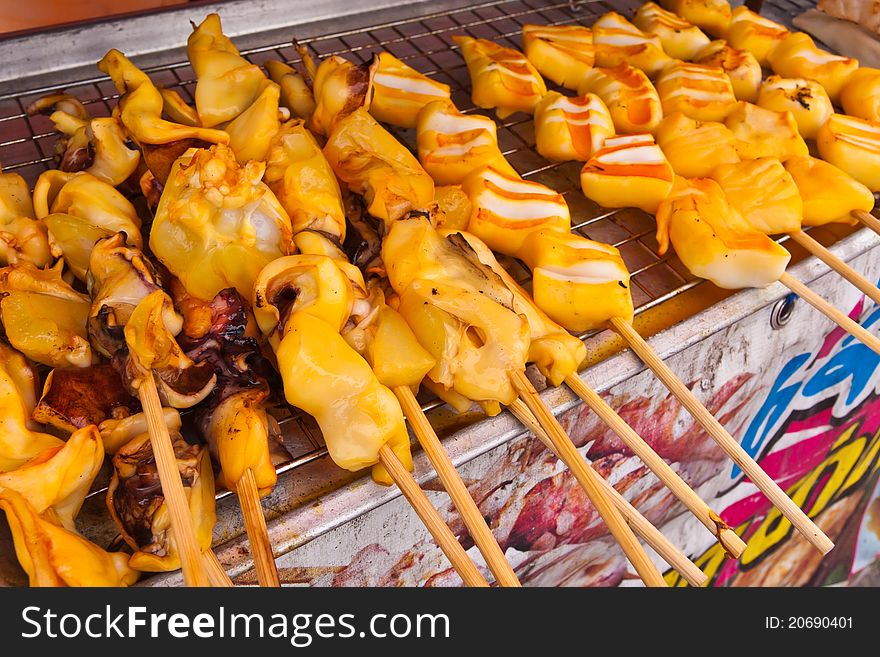 Yellow grilled squids in group with wooden stick on grill. Yellow grilled squids in group with wooden stick on grill