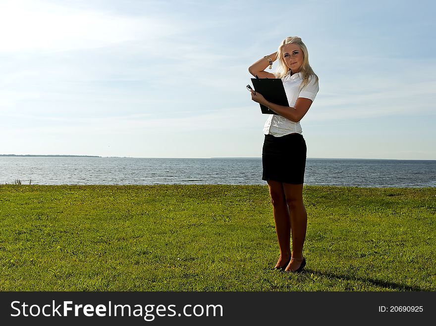 Girl standing with a folder on the background of the sea, sky and grass. Girl standing with a folder on the background of the sea, sky and grass