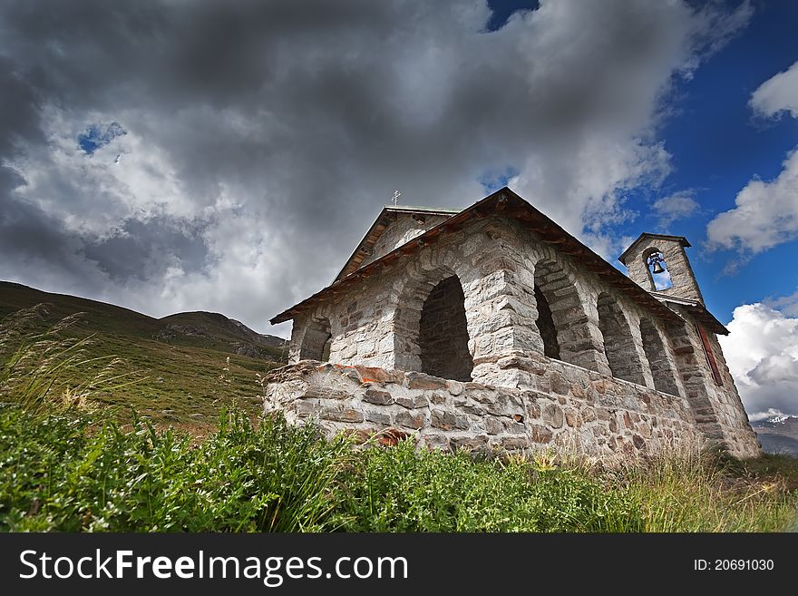 A small church in high mountain during summer with a cloudy sky