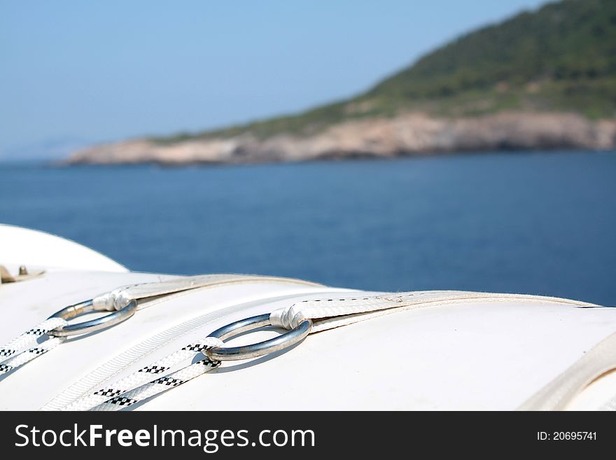 Focus on metal rings of a lifeboat, in front of a island