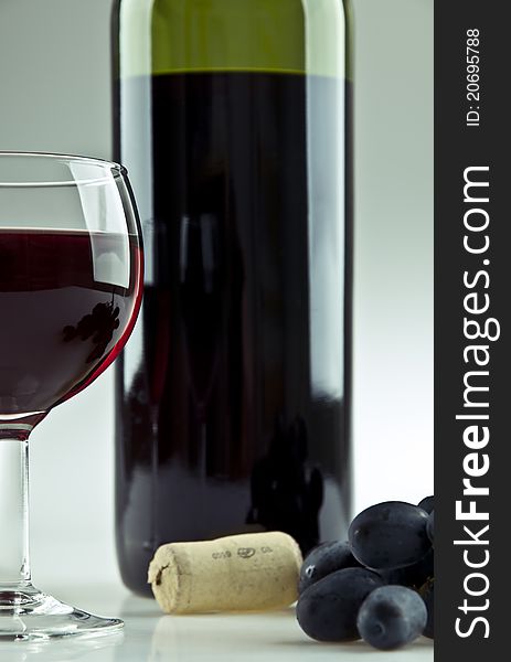 A glass, a cork, some grapes and a bottle of red wine. A glass, a cork, some grapes and a bottle of red wine