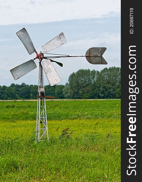 An old Dutch windmill with windvane in the field pumping water from the ditch. An old Dutch windmill with windvane in the field pumping water from the ditch