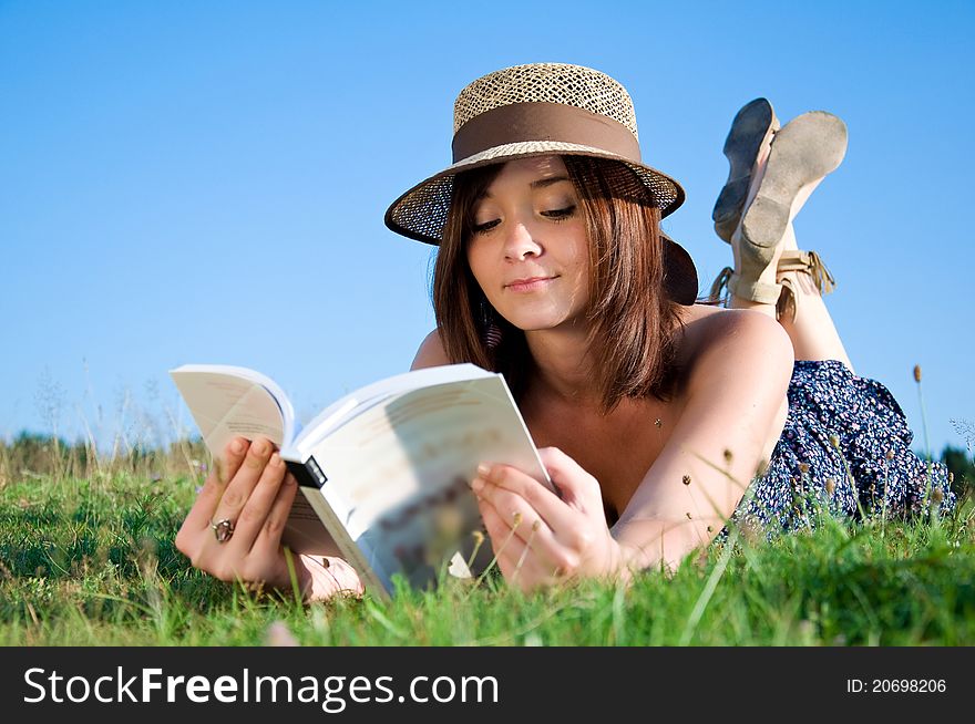Young nice attentive woman lies on green grass and reads book
