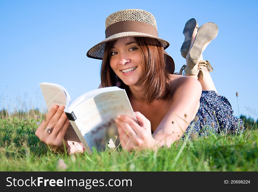 Young nice attentive woman lies on green grass and reads book