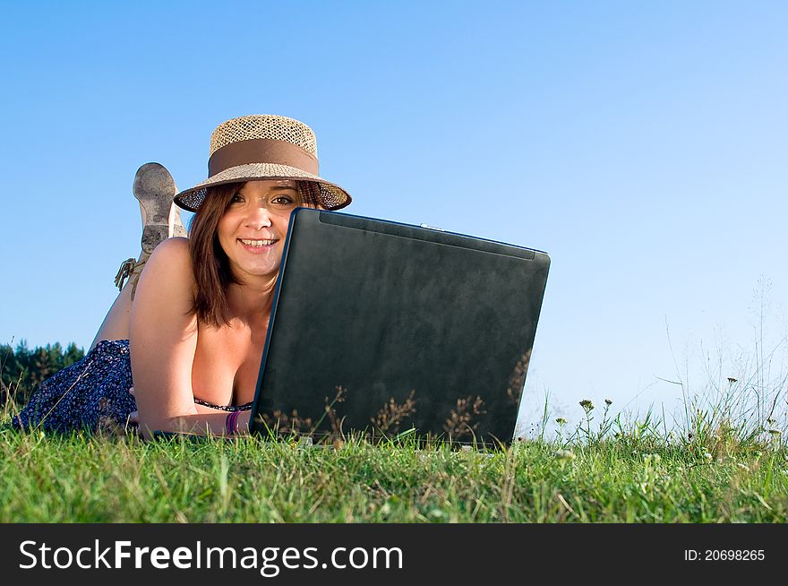 Smiling beautiful woman laying on grass and working on laptop