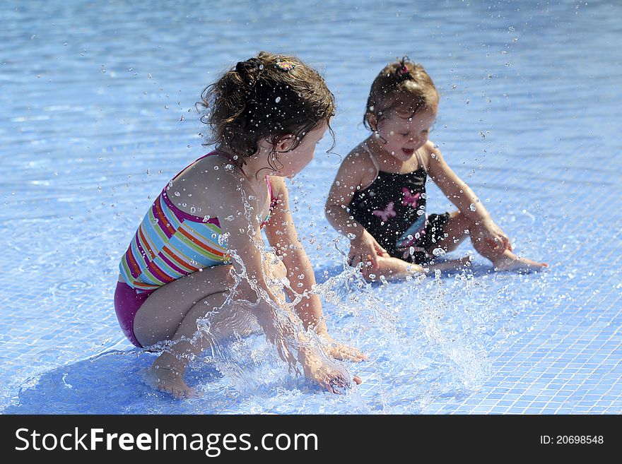 Two small sisters are playing in the swimming pool