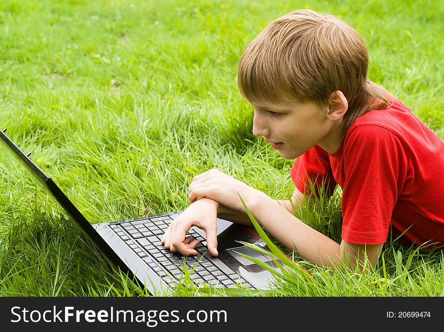 Young boy with laptop lying on grass