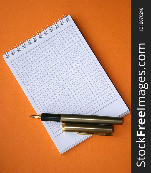 Notebook with a spiral with a place for the text and a pen on an orange background. Notebook with a spiral with a place for the text and a pen on an orange background.