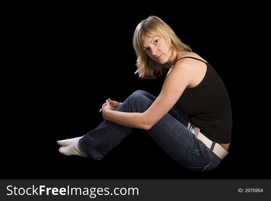 Young blond woman sitting lateral on the bottom with black background. Young blond woman sitting lateral on the bottom with black background