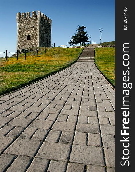 A tower along a stone road with green/yellow grass and a clear blue sky. A tower along a stone road with green/yellow grass and a clear blue sky.