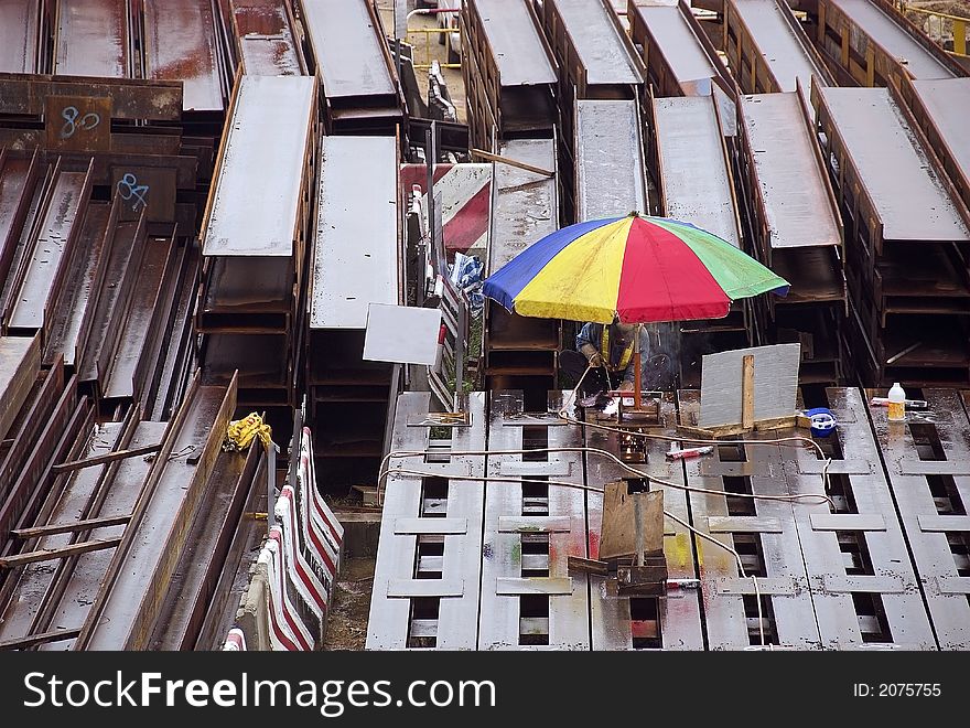Worker in Hong Kong welding steel girders under an umbrella while it is raining. Worker in Hong Kong welding steel girders under an umbrella while it is raining