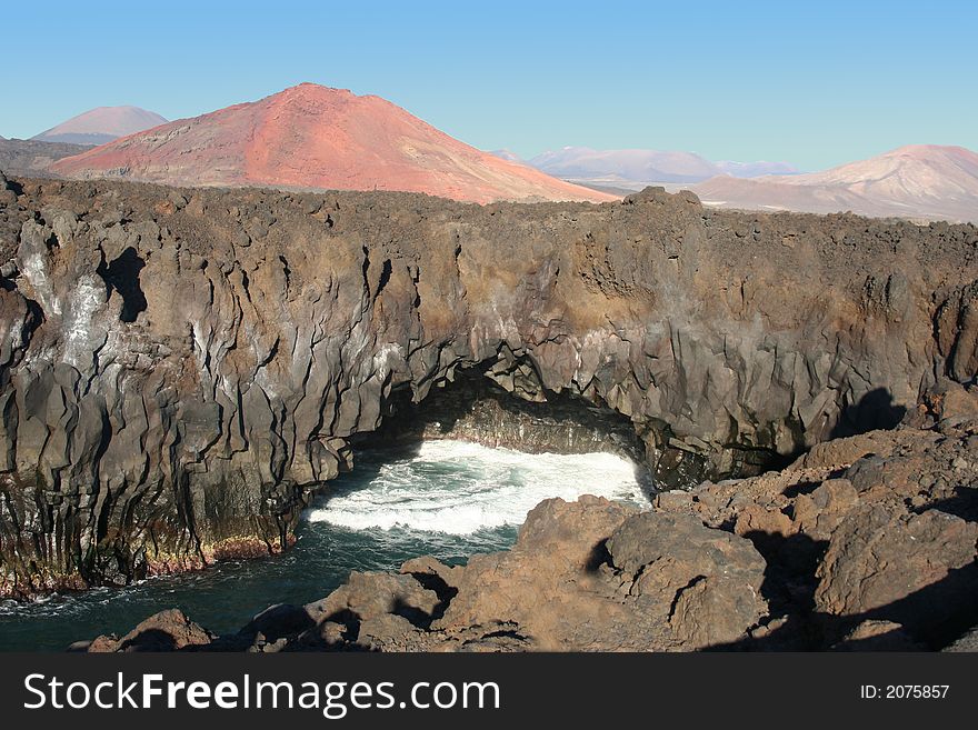 Volcanic rocks by the water and red montain. Volcanic rocks by the water and red montain