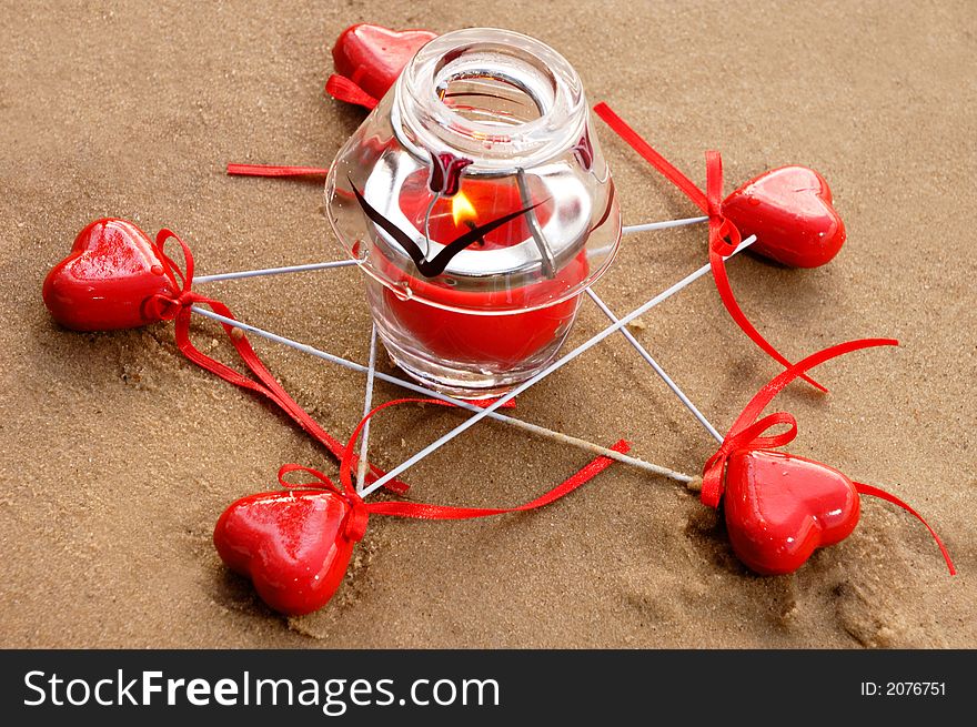 Five pointed star made from red hearts and a burning candle on sand conceptual still life. Five pointed star made from red hearts and a burning candle on sand conceptual still life