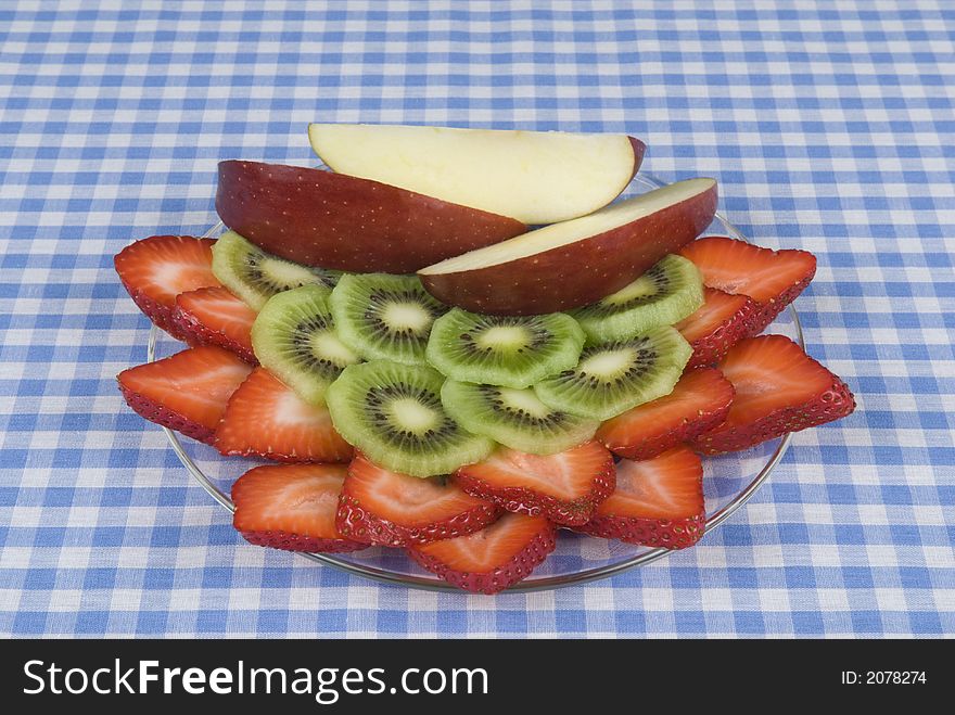 Apples, strawberry, kiwi fruit dish on a blue and white checkerboard cloth