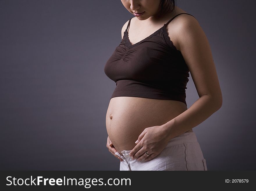 Studio shot of a pregnant woman standing over grey background with her stomach exposed. Studio shot of a pregnant woman standing over grey background with her stomach exposed