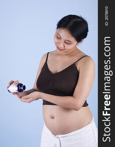 Studio shot of a pregnant woman taking vitamin over blue background with her stomach exposed. Studio shot of a pregnant woman taking vitamin over blue background with her stomach exposed