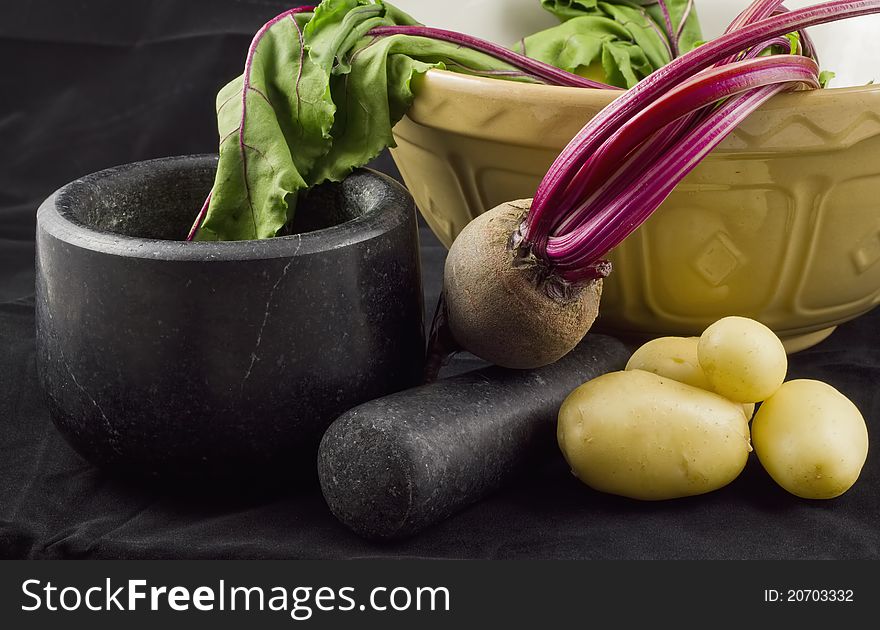 A photo of some potatoes, a beetroot, a mortar & pestle, and a crockery bowl. Shot on black velvet. A photo of some potatoes, a beetroot, a mortar & pestle, and a crockery bowl. Shot on black velvet.