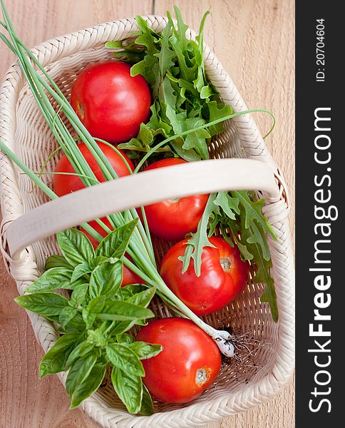 Farm fresh tomatoes, basil, scallions, and lettuce rest in a woven basket. Farm fresh tomatoes, basil, scallions, and lettuce rest in a woven basket.