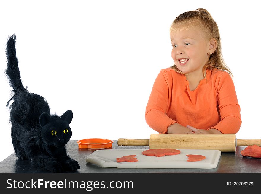 An adorable preschooler skittish with a furry black cat while making Halloween cookies from orange modeling clay. An adorable preschooler skittish with a furry black cat while making Halloween cookies from orange modeling clay.