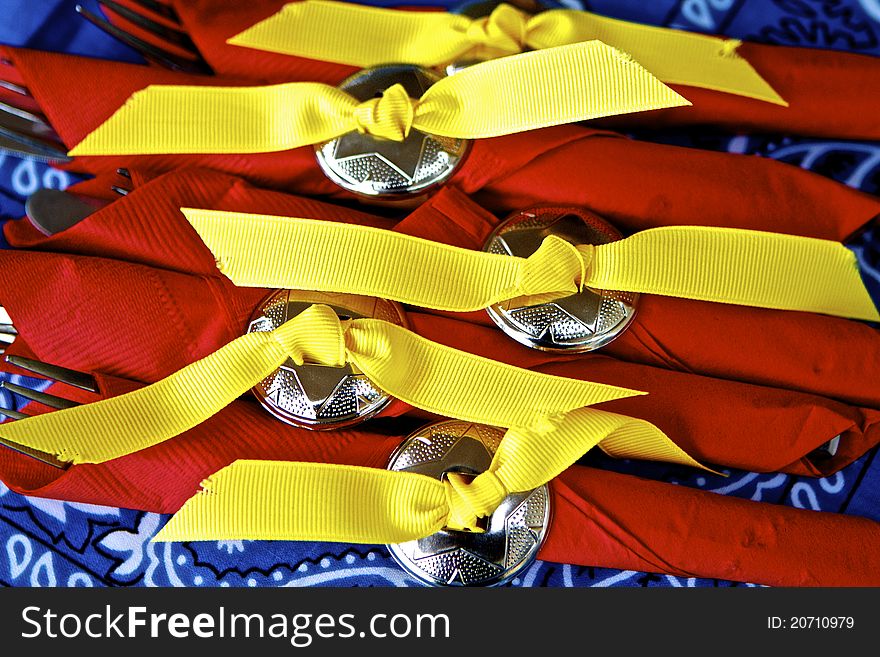 Striking yellow-ribboned silver disks holding red napkins atop blue bandana. Striking yellow-ribboned silver disks holding red napkins atop blue bandana