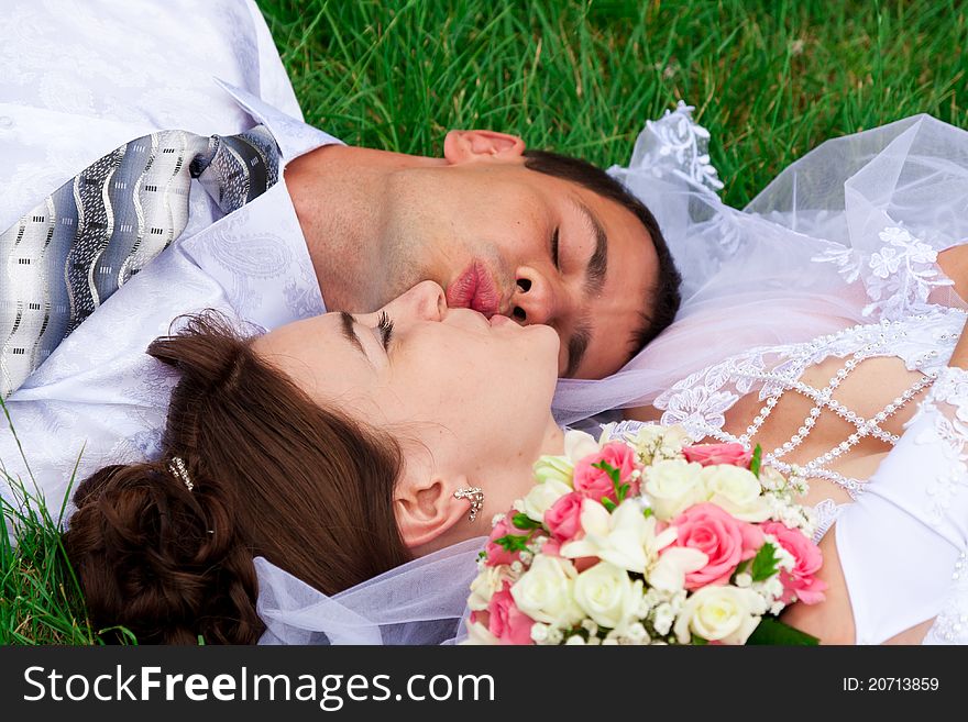 Happy smiling bride and groom  lying on a green grass kissing. Happy smiling bride and groom  lying on a green grass kissing