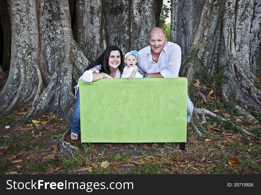 A portrait of a happy young family leaning over back of a love seat under a tree. A portrait of a happy young family leaning over back of a love seat under a tree.