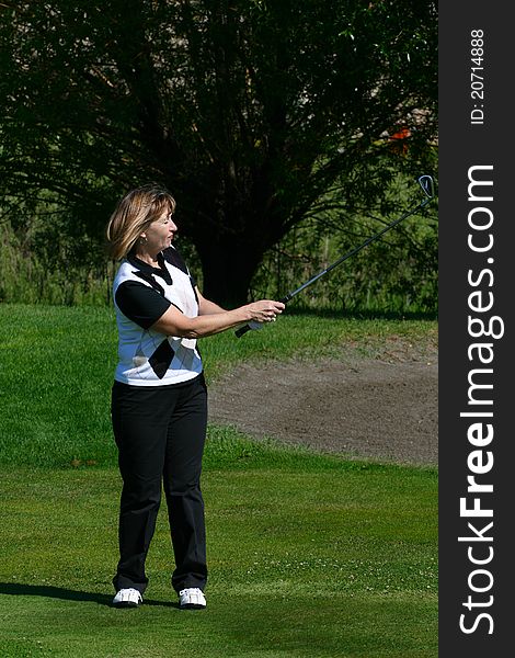 Adult female golfer playing an iron shot from the fairway. Adult female golfer playing an iron shot from the fairway
