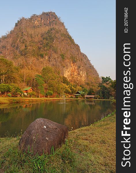 Landscape view of towering mountain behind pond with golden sunset rays.