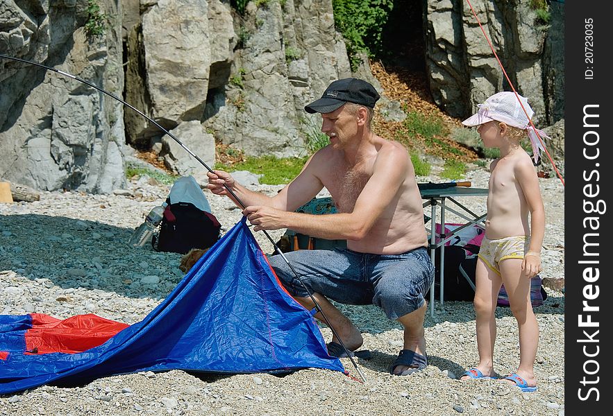 Father and daughter put a tent next to the rocks