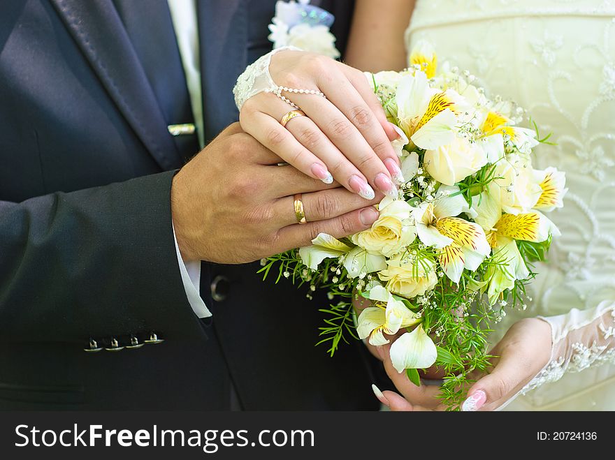 Hands of bride and groom with wedding rings over the bridal bouquet. Hands of bride and groom with wedding rings over the bridal bouquet