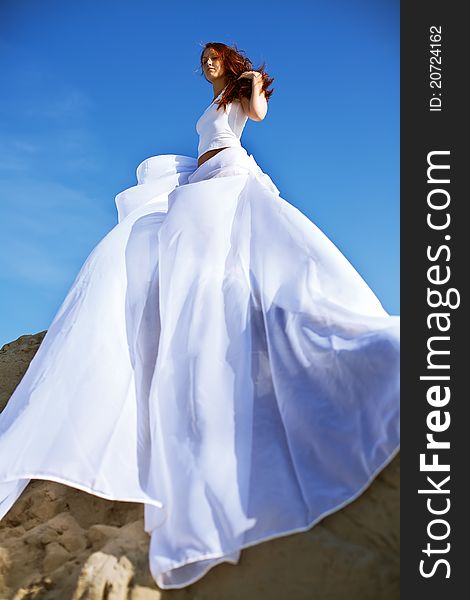 Young blond woman in white dress on background of the sky